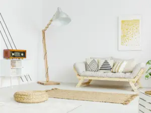 A modern living room with a light wood futon sofa, neutral patterned cushions, a tall floor lamp, woven rug, pouf, and wall art with yellow dots&mdash;perfect for enjoying stylish comfort in real estate properties Ulcinj Montenegro ekosphere.