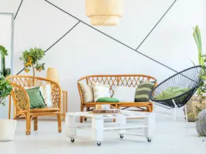A bright living room in Ulcinj, Montenegro, with rattan furniture, green and white cushions, a black modern chair, a white wooden coffee table on wheels, potted plants, and a white wall with geometric black lines&mdash;perfect for ekosphere real estate properties.