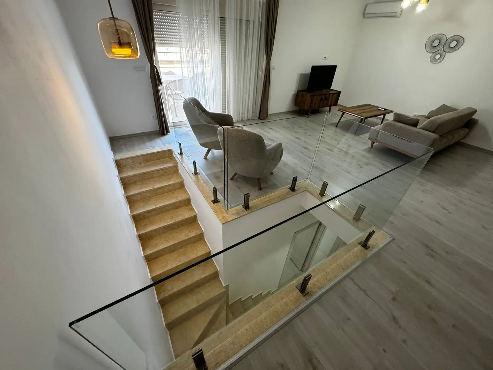 Bright modern living room with light wood floors, designer furnishings, and large windows&mdash;ideal Ulcinj investment via immorenta.me by ekosphere doo.