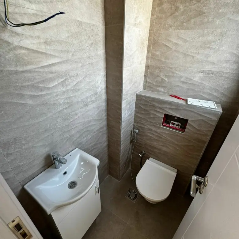 Stylish modern bathroom in Ulcinj, Montenegro&mdash;beige tiles, wall toilet, sink cabinet; ideal investment via immorenta.me (EkoSphere).