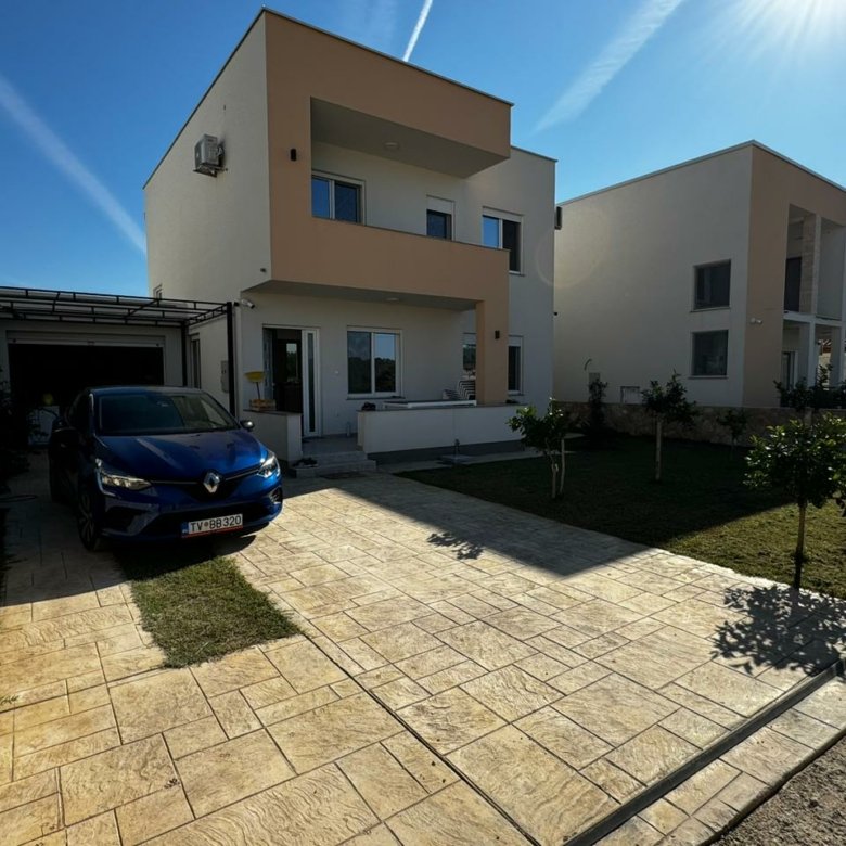 Modern two-story cream and white home in Ulcinj, Montenegro, with driveway, carport, green lawn; exclusive at immorenta.me by Ekosphere doo.