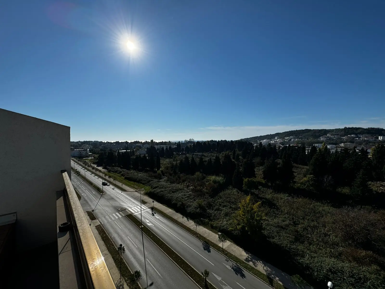 Bright balcony view in Ulcinj, Montenegro with lush greenery, clear sky, and quiet road&mdash;ideal for prime real estate investment. Powered by ekosphere doo via immorenta.me.