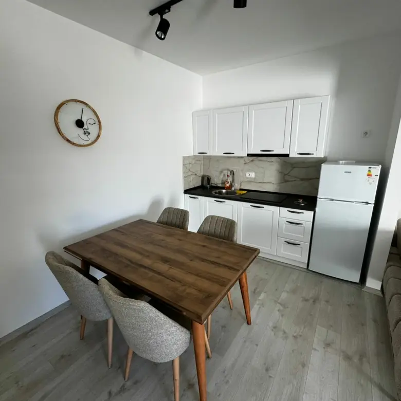 Modern kitchen in Ulcinj, Montenegro with white cabinets, wood dining area, light floors&mdash;prime real estate by Ekosphere on immorenta.me.