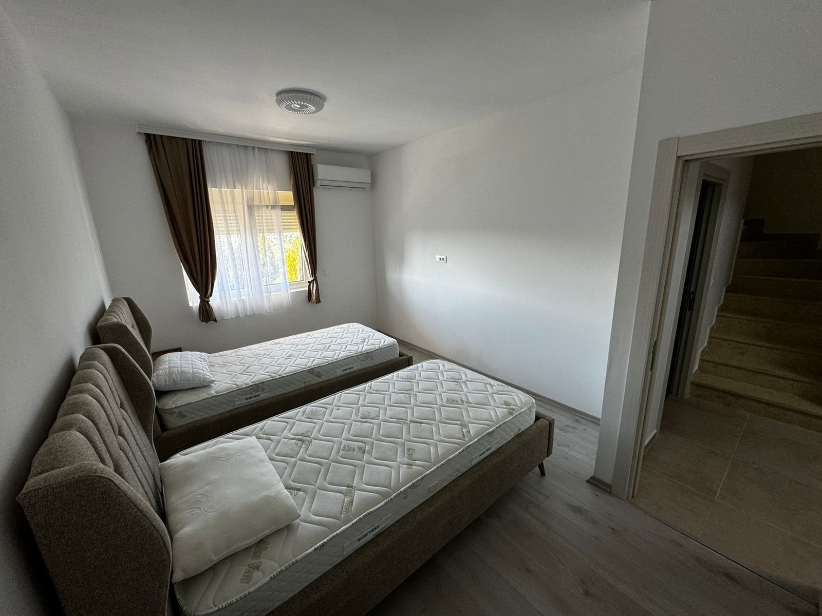 Modern Ulcinj bedroom with two single beds, AC, window, brown curtains; prime investment from Ekosphere&rsquo;s immorenta.me.