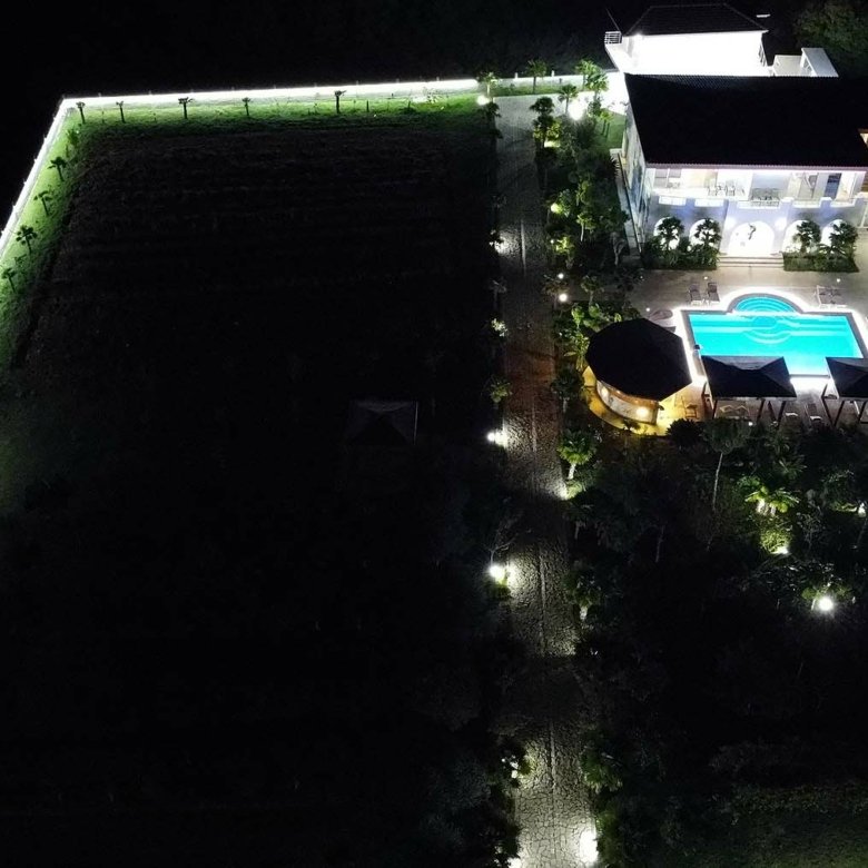 Stunning aerial night view: luxury modern home with pool, lush gardens, and illuminated fencing in Ulcinj Montenegro. An exclusive immorenta.me by ekosphere doo property investment opportunity.