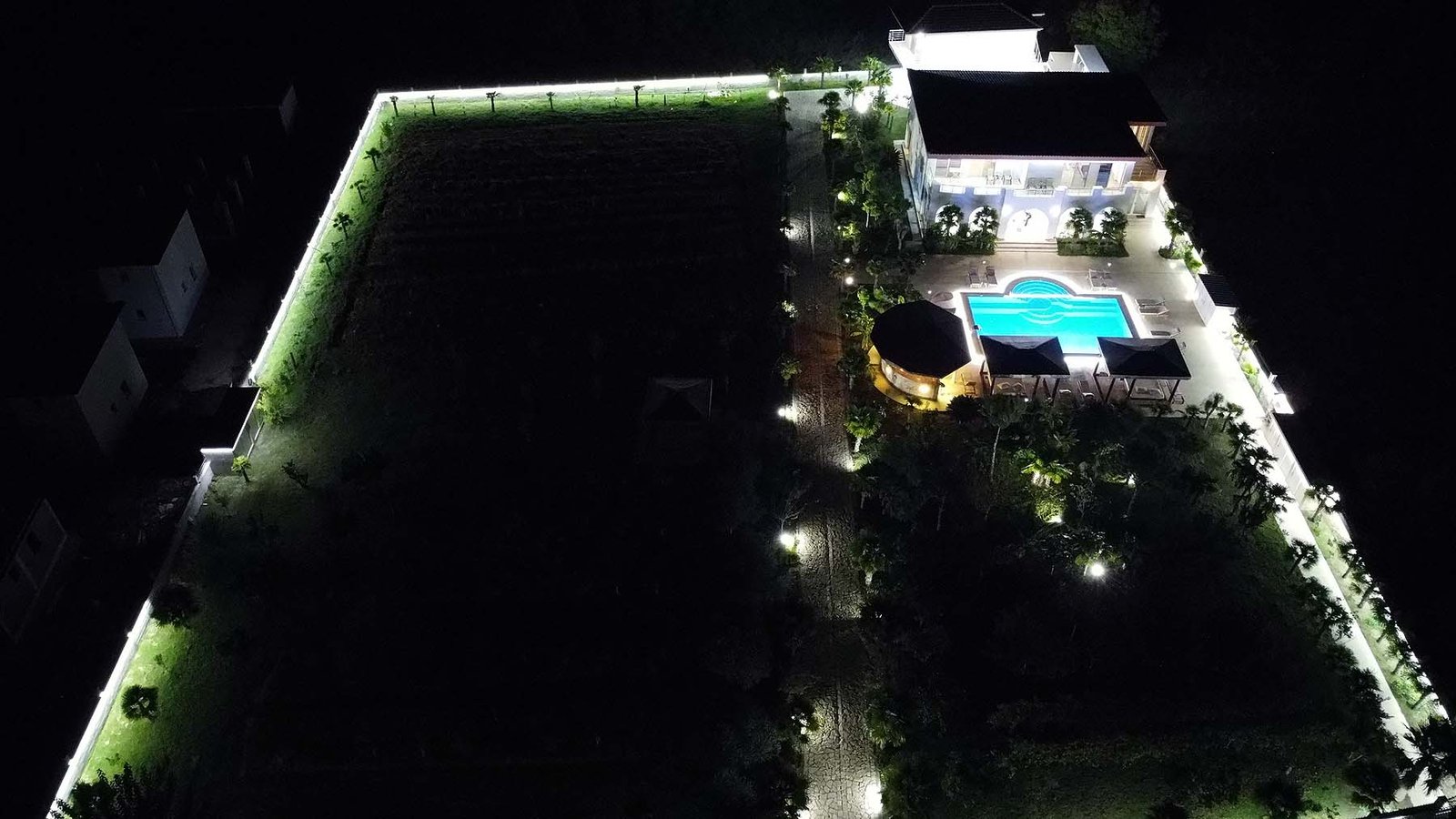 Stunning aerial night view: luxury modern home with pool, lush gardens, and illuminated fencing in Ulcinj Montenegro. An exclusive immorenta.me by ekosphere doo property investment opportunity.