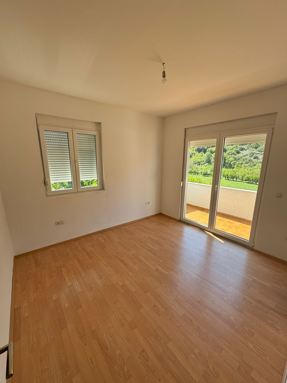 Invest in Ulcinj: bright room with wood floors, white walls, balcony & green views. Listed by immorenta.me (ekosphere doo).