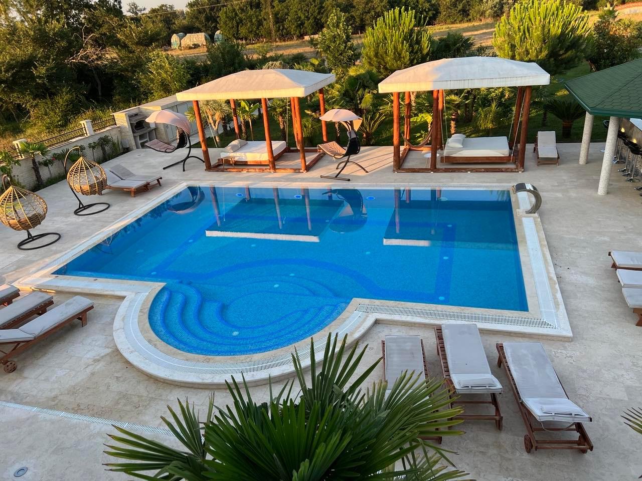 Luxurious pool oasis with blue tiles, lounge chairs, cabanas & chic seating&mdash;prime Ulcinj investment. Listed on immorenta.me.