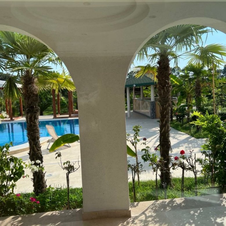 Stunning Ulcinj villa for sale: tropical garden, palm trees, pool view through white arches. Invest via immorenta.me by Ekosphere Doo.