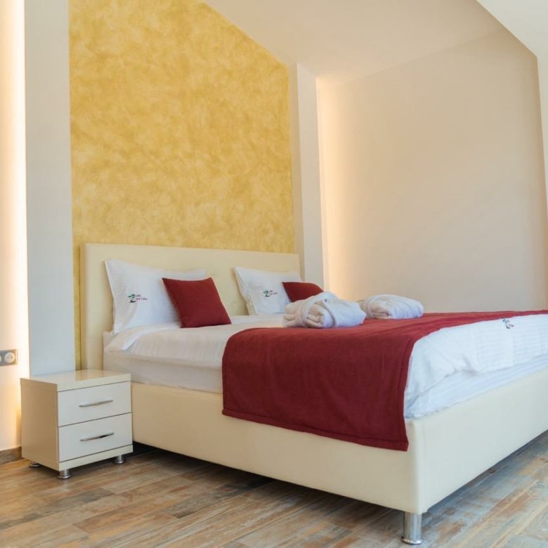 Elegant Ulcinj bedroom with double bed, white linens, yellow accent wall, and wood floors&mdash;prime Montenegro real estate by ekosphere.