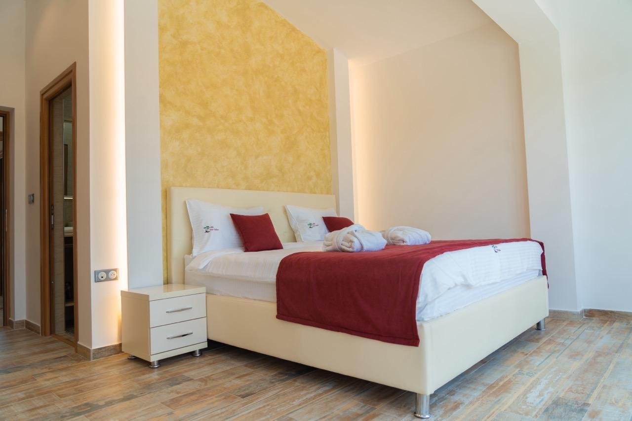 Elegant Ulcinj bedroom with double bed, white linens, yellow accent wall, and wood floors&mdash;prime Montenegro real estate by ekosphere.