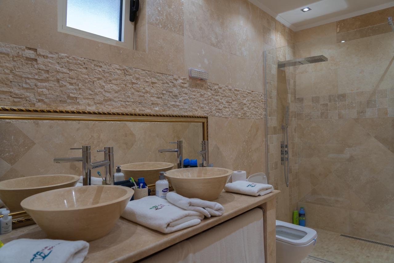 Luxury bathroom in Ulcinj, Montenegro: beige stone, double sinks, walk-in glass shower&mdash;exclusive Ekosphere/ immorenta.me property.