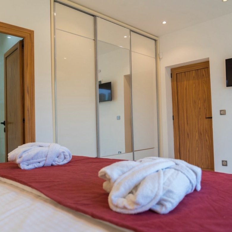 Modern Ulcinj property: elegant bedroom with red coverlet, bathrobes, premium finishes. Exclusive on immorenta.me by Ekosphere DOO.