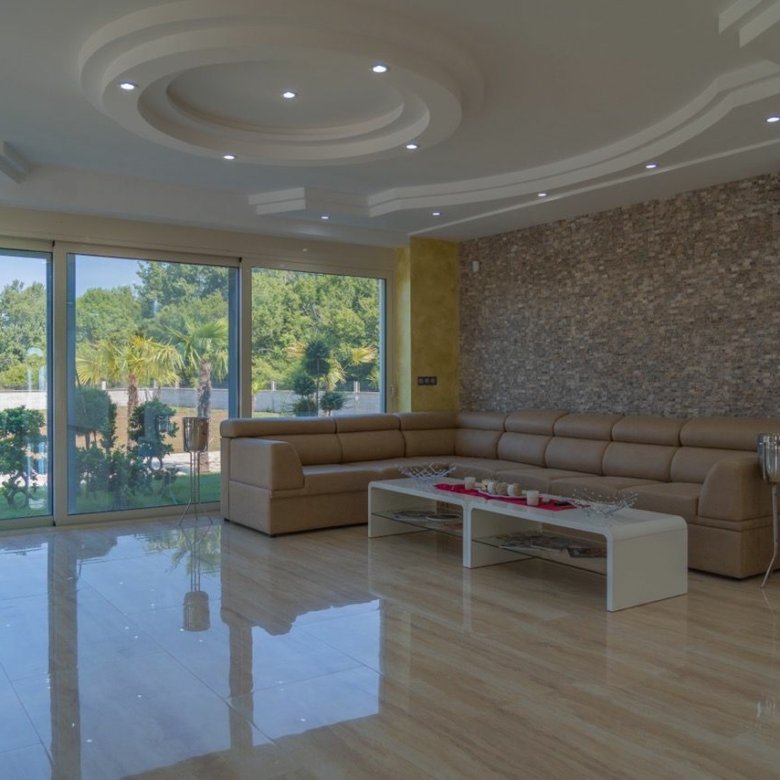 Modern Ulcinj living room with tan sectional, white coffee table, stone accent wall, and lush views&mdash;exclusive by immorenta.me.