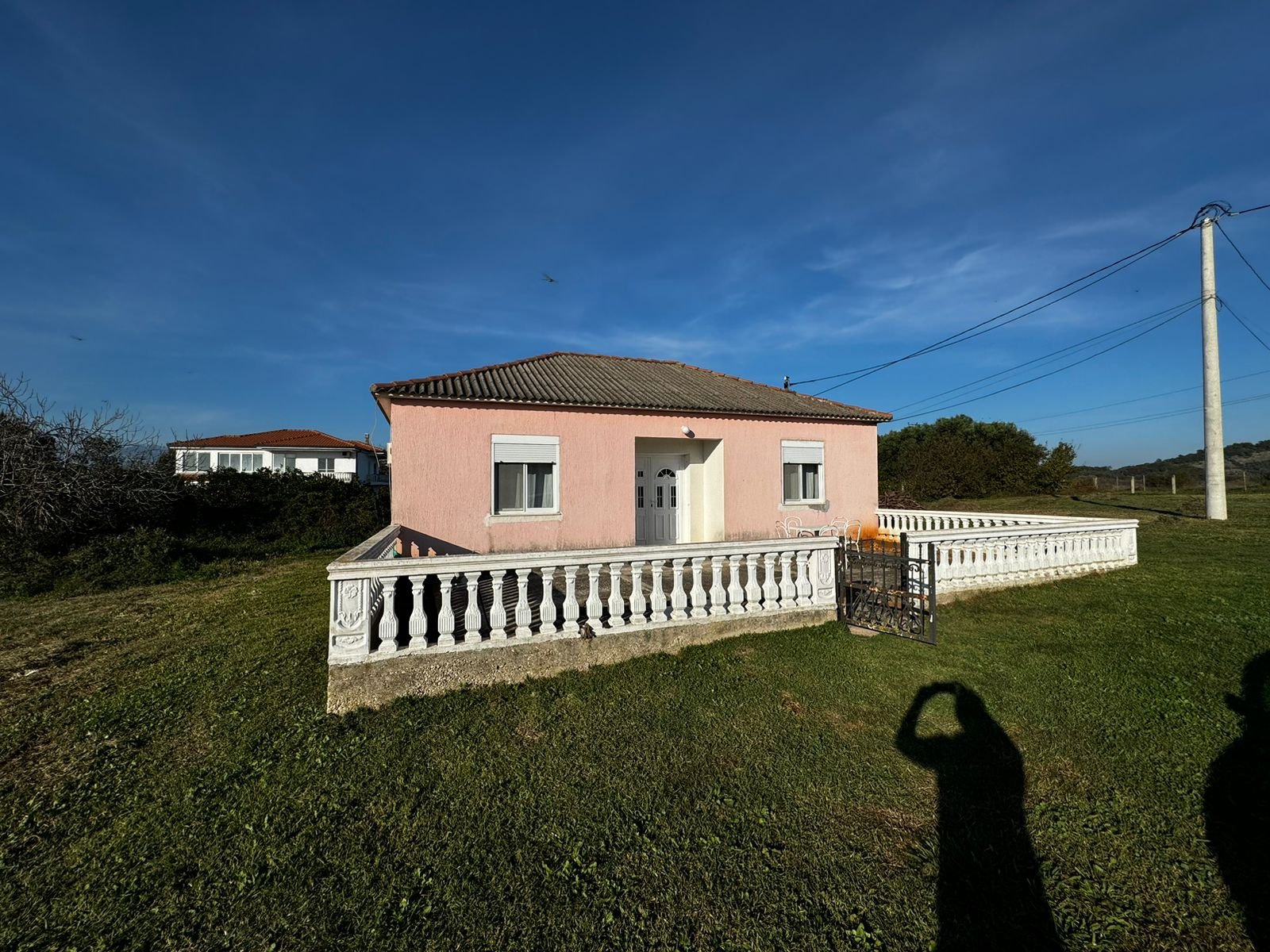 Charming single-story pink home with tiled roof, white fence, and gated lawn in Ulcinj. Exclusive at immorenta.me by ekosphere doo.