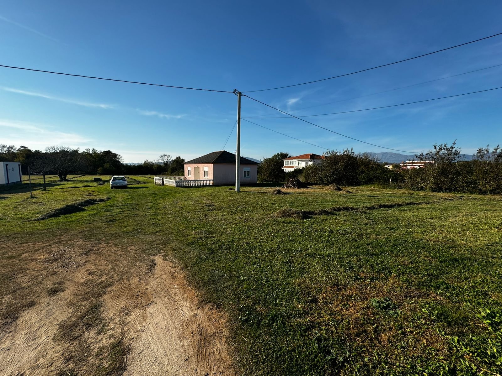 Spacious grassy yard with path, car, and charming pink house&mdash;prime Ulcinj real estate. Montenegro-Listings.me by Ekosphere DOO.