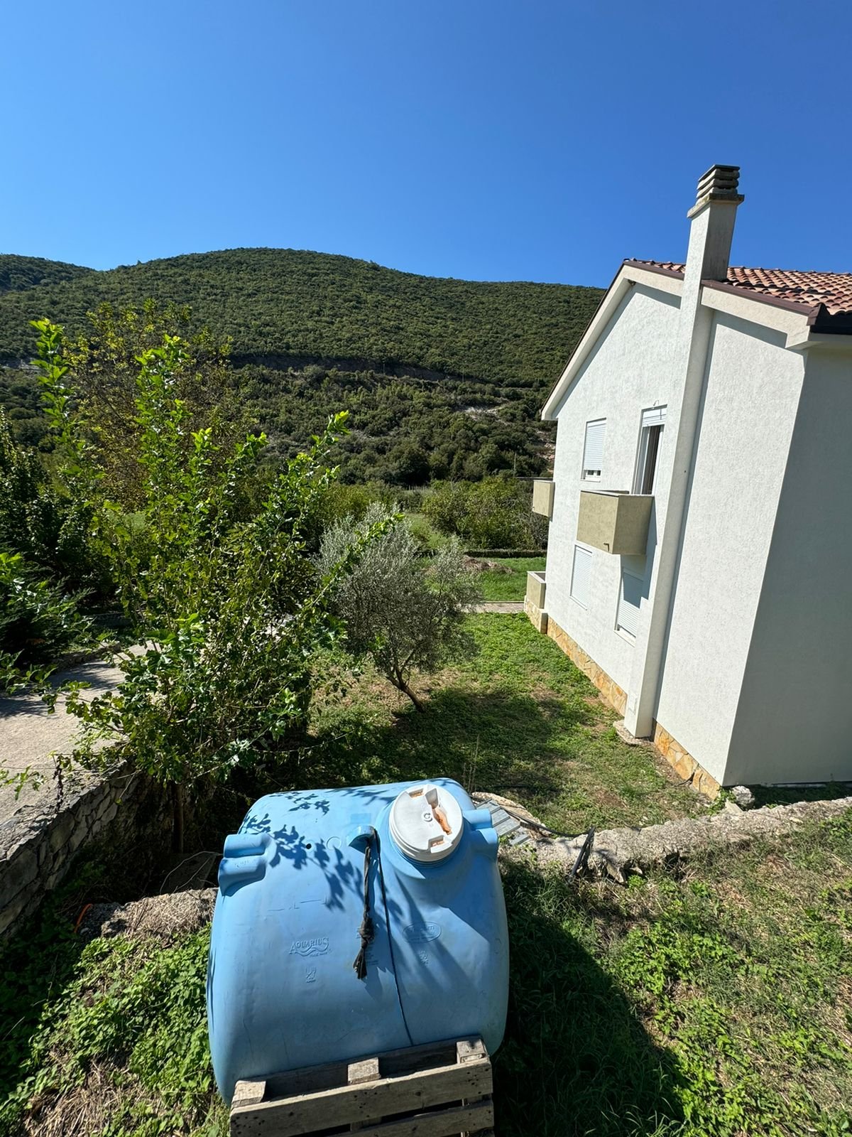 Charming white house with red roof, water tank, lush greenery, hills&mdash;prime Ulcinj real estate by ekosphere doo on immorenta.me.