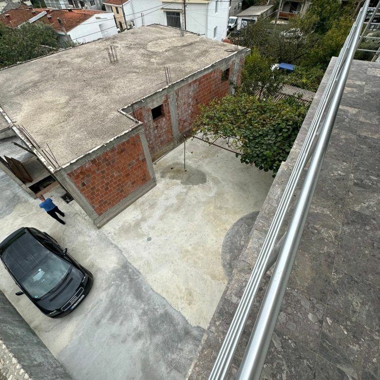 Balcony view of courtyard, black car, new brick construction & lush trees&mdash;prime Ulcinj investment. Listed on immorenta.me by ekosphere doo.