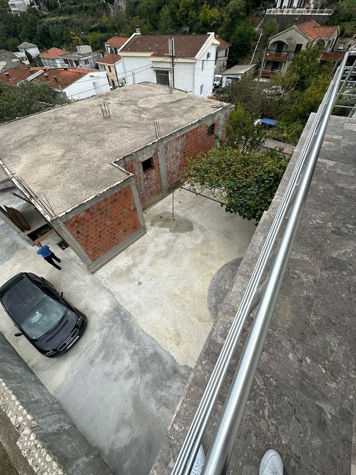 Balcony view of courtyard, black car, new brick construction & lush trees&mdash;prime Ulcinj investment. Listed on immorenta.me by ekosphere doo.