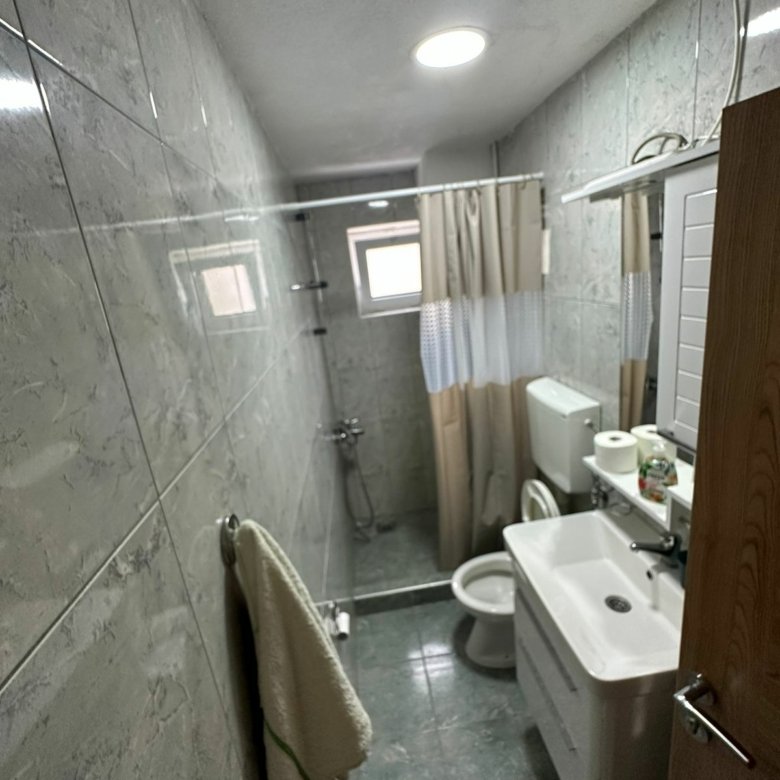 Modern gray-tiled bathroom with shower, toilet, sink, and mirror in Ulcinj property&mdash;exclusive on immorenta.me by ekosphere doo.