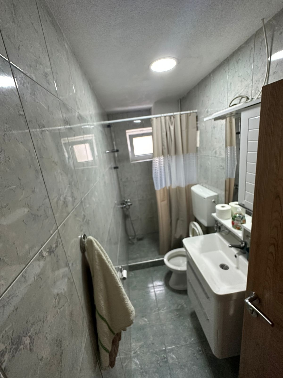 Modern gray-tiled bathroom with shower, toilet, sink, and mirror in Ulcinj property&mdash;exclusive on immorenta.me by ekosphere doo.