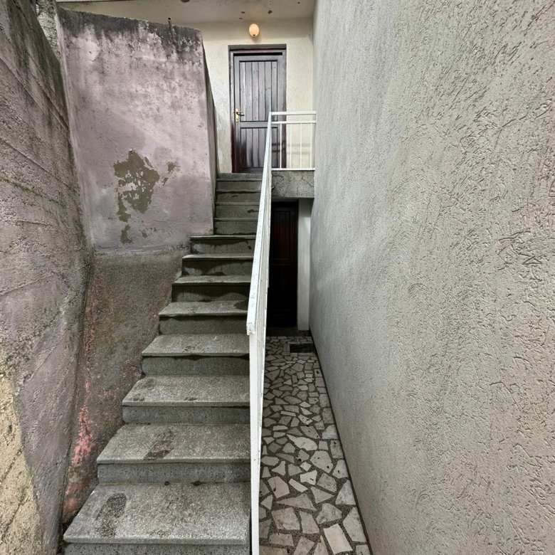 Prime Ulcinj property: concrete stairs, white railing, dual dark brown doors, stone path, and weathered fa&ccedil;ade. Invest via immorenta.me by ekosphere doo.