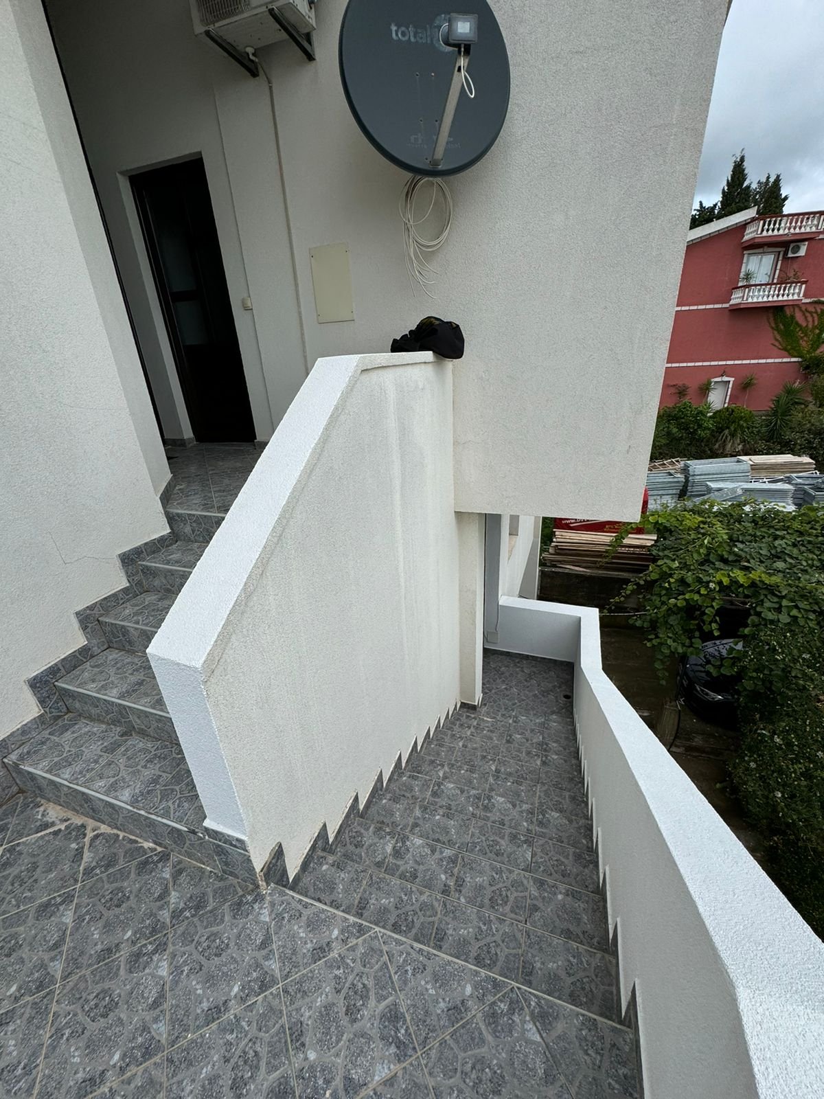 Premium Ulcinj property: tiled stairs, white wall with satellite, red building and lush greenery. immorenta.me by ekosphere doo.