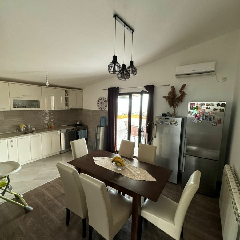 Stylish Ulcinj kitchen with wooden table, white chairs, sleek cabinets, and glass door&mdash;prime eco-investment at immorenta.me.