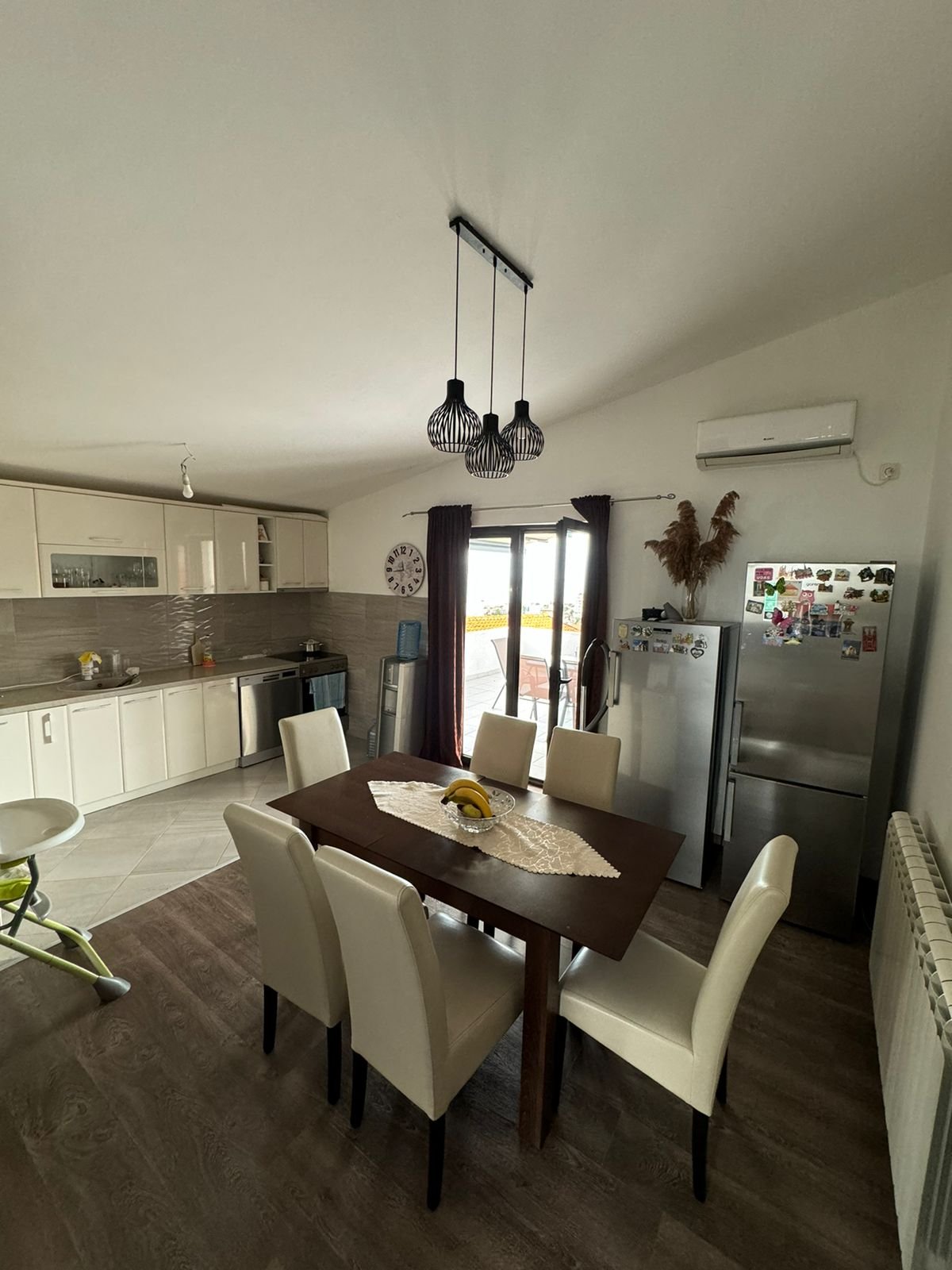 Stylish Ulcinj kitchen with wooden table, white chairs, sleek cabinets, and glass door&mdash;prime eco-investment at immorenta.me.