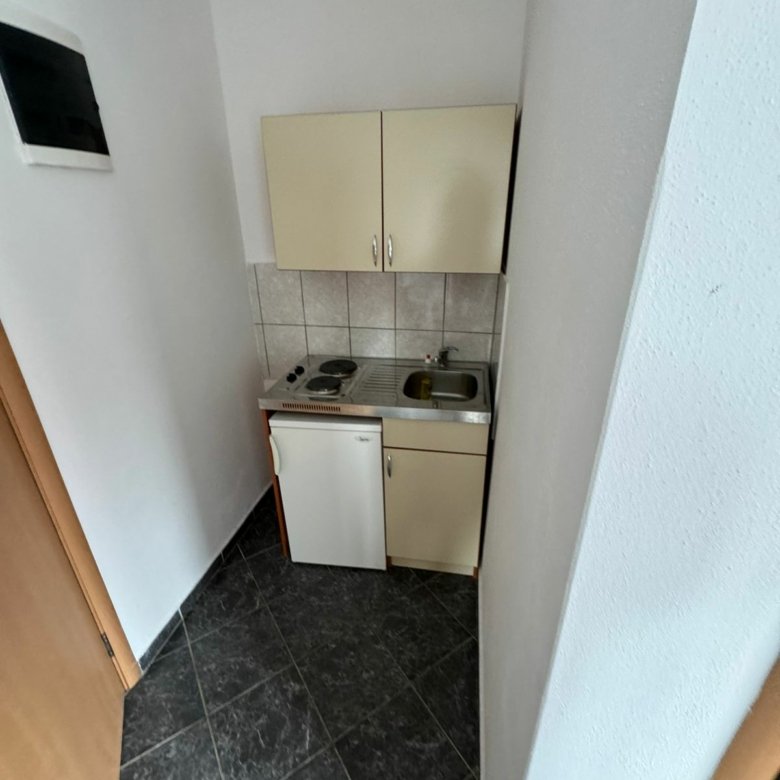 Modern kitchenette in Ulcinj: sleek tiled backsplash, white cabinets, mini fridge, stove. Ideal Montenegro property&mdash;by ekosphere doo.