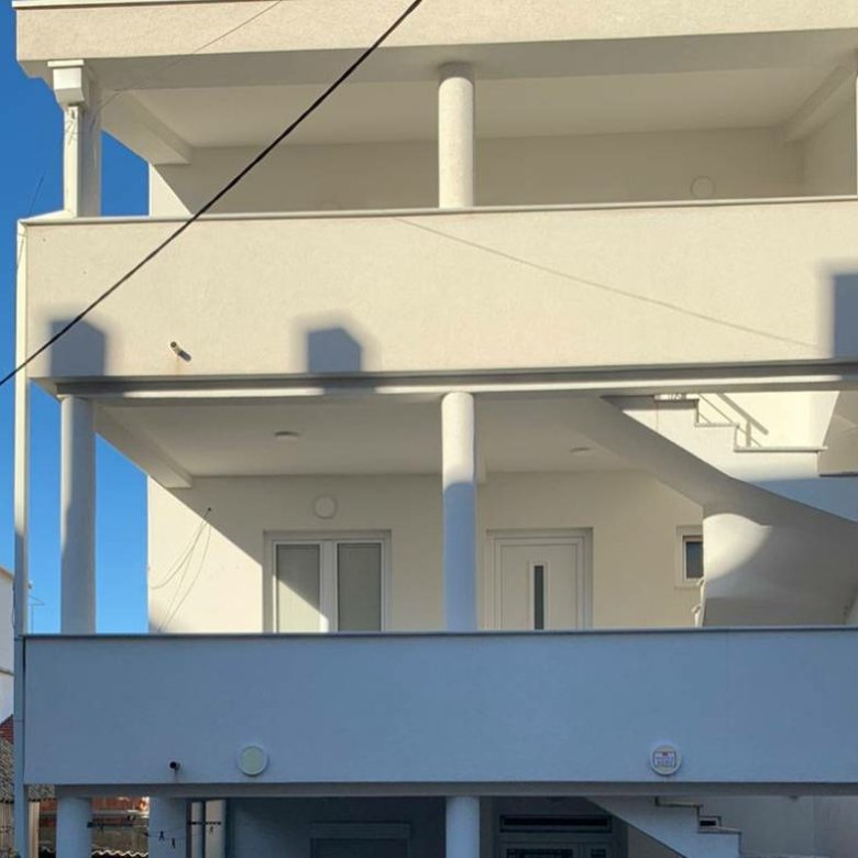 Elegant three-story white property with balconies, pillars, and spiral staircase in sunny Ulcinj. Exclusive on immorenta.me by ekosphere doo.