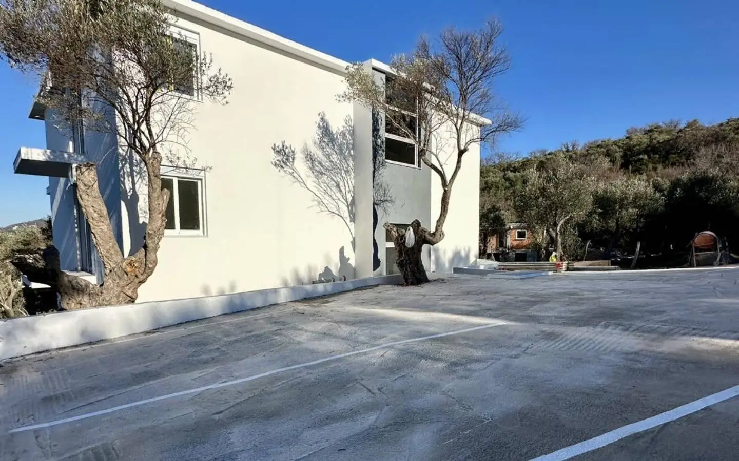 Modern white building with parking, lush greenery, and blue sky&acirc;prime Ulcinj real estate. Listed on immorenta.me by ekosphere doo.