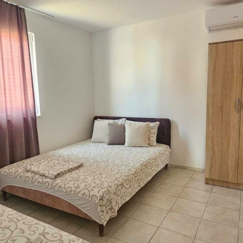 Modern Ulcinj bedroom with 2 beds, wardrobe, TV, window with pink curtains&mdash;prime real estate by Ekosphere on immorenta.me.