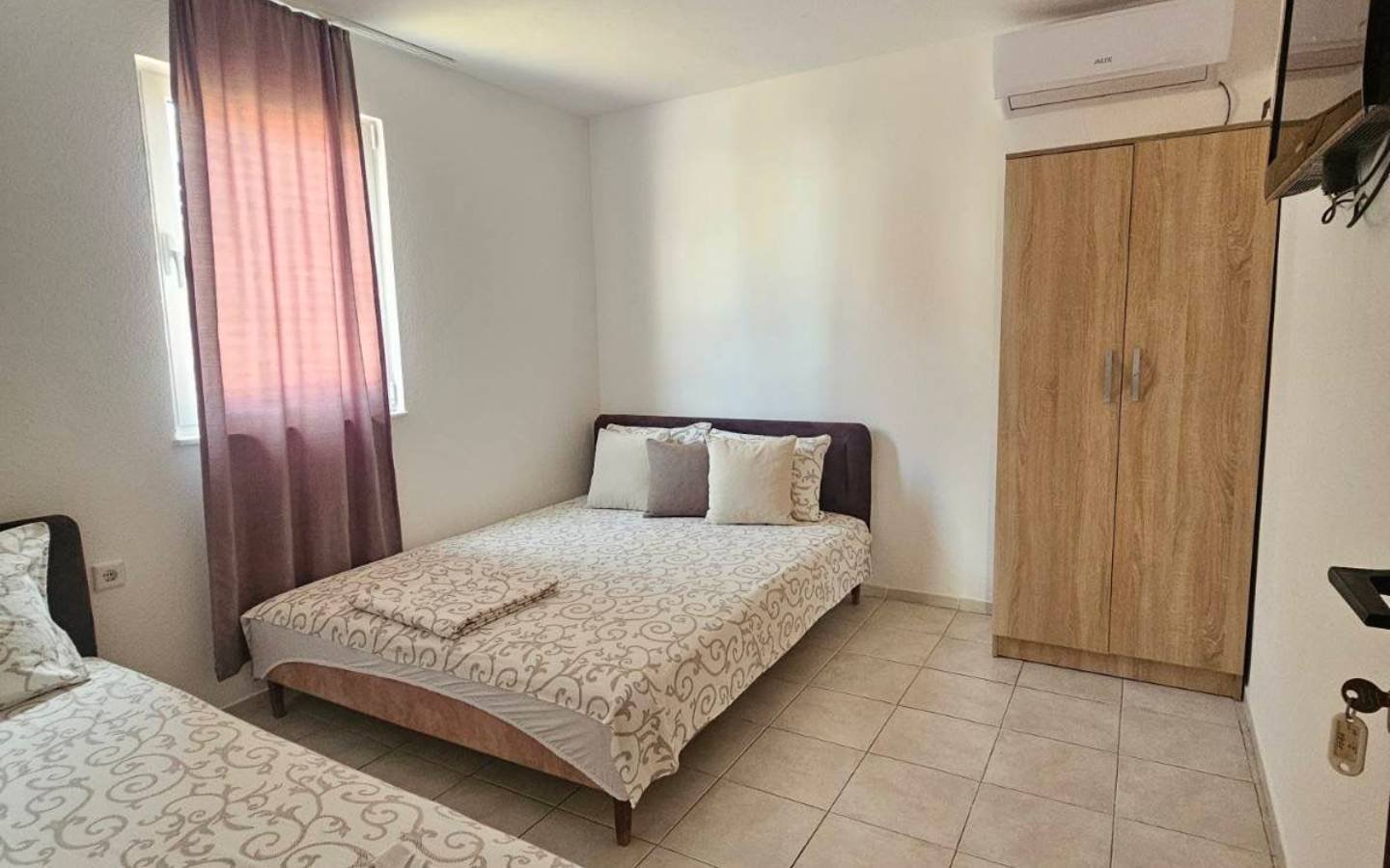 Modern Ulcinj bedroom with 2 beds, wardrobe, TV, window with pink curtains&mdash;prime real estate by Ekosphere on immorenta.me.