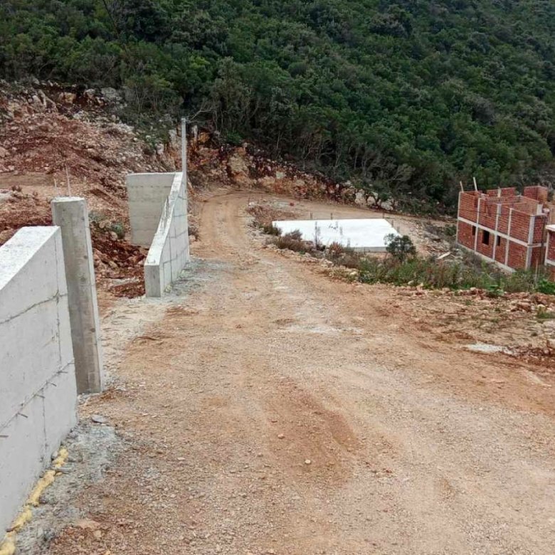 Prime investment opportunity in Ulcinj: sloping access, concrete wall, and unfinished brick homes with lush hillside views. Montenegro-listings.me by ekosphere doo.