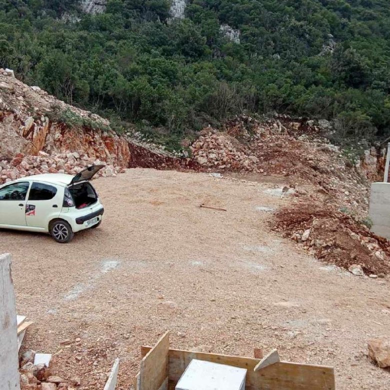 White car with open trunk parked on gravel site in Ulcinj, Montenegro&mdash;ideal for real estate investment. By ekosphere doo.