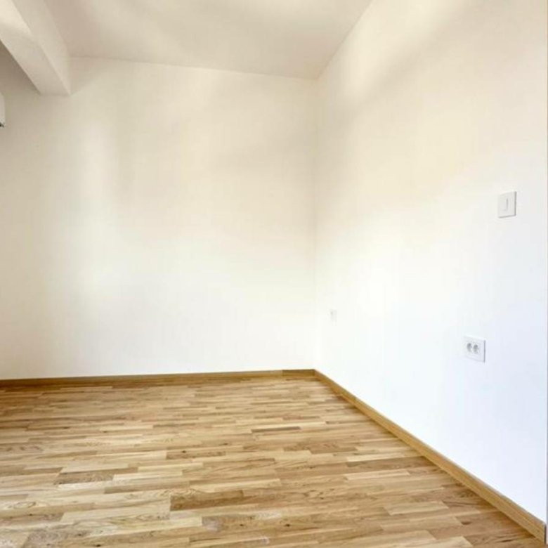 Modern, sunlit room with wooden flooring, white walls, AC, ideal Ulcinj investment. Listed on immorenta.me by Ekosphere.