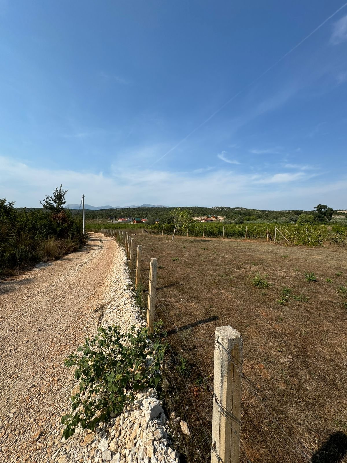 Stunning Ulcinj land for sale: gravel road, fenced plots, scenic hills, red-roof homes&mdash;exclusive from ekosphere doo at immorenta.me.