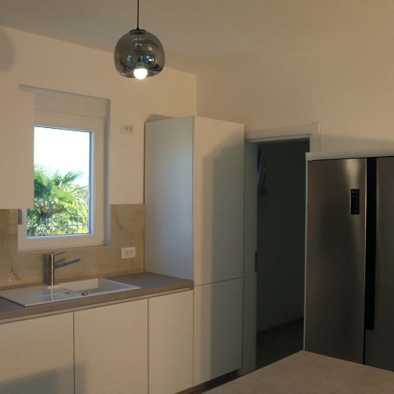 Bright modern kitchen in Adana Villa, Ulcinj: sleek white cabinets, stainless fridge, sunny window&mdash;exclusive from immorenta.me by ekosphere doo.