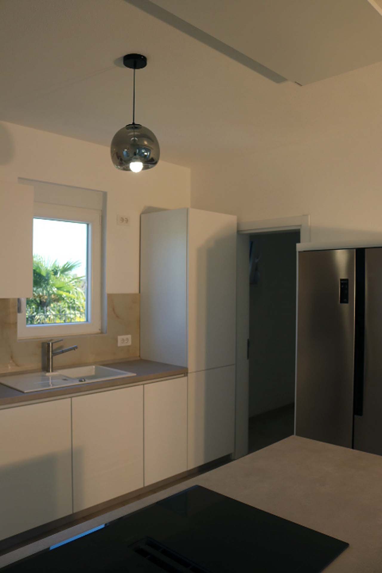 Bright modern kitchen in Adana Villa, Ulcinj: sleek white cabinets, stainless fridge, sunny window&mdash;exclusive from immorenta.me by ekosphere doo.