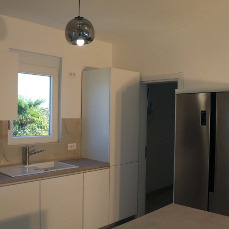 Stunning Ulcinj villa kitchen: sleek white cabinets, stainless fridge, sunlit space. Prime Montenegro investment at immorenta.me.