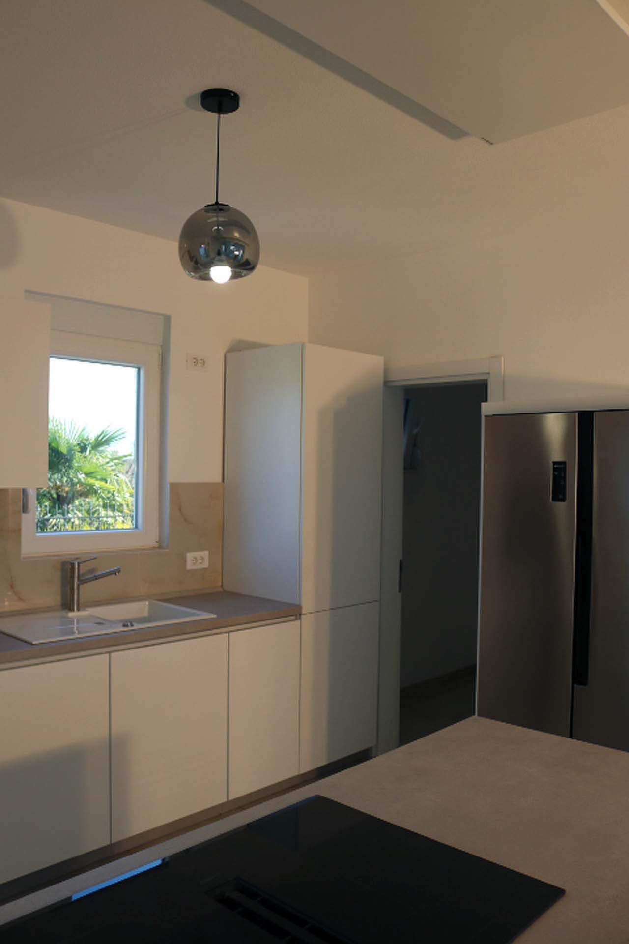 Stunning Ulcinj villa kitchen: sleek white cabinets, stainless fridge, sunlit space. Prime Montenegro investment at immorenta.me.