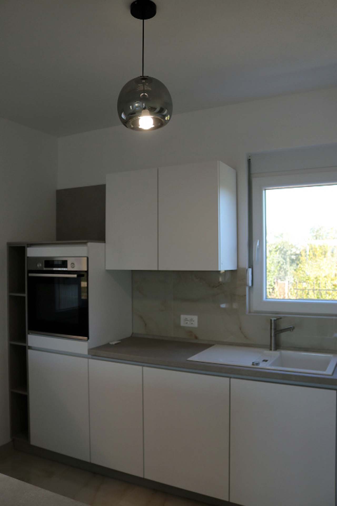 Stylish Adana Villa kitchen in Ulcinj: white cabinets, built-in oven, windowed sink, grey countertops&mdash;exclusive at immorenta.me by ekosphere doo.