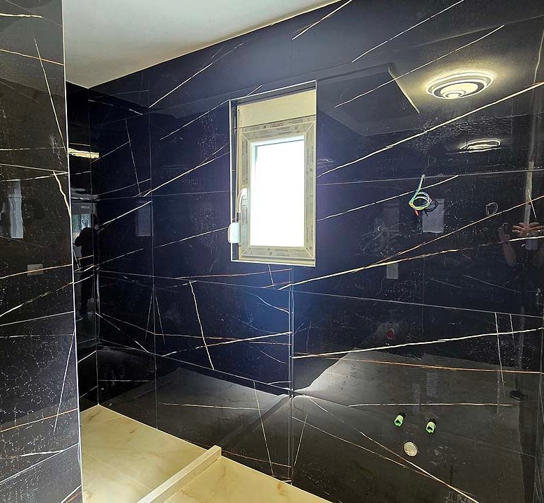 Modern Ulcinj bathroom with black marble walls, white fixtures, and natural light&mdash;exclusive at immorenta.me by Ekosphere.