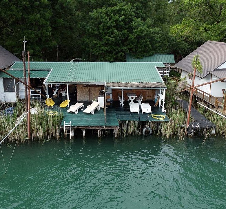 Stylish riverside deck with white seating, lush greenery, and eco-inspired buildings&mdash;premier Ulcinj real estate via ekosphere doo.