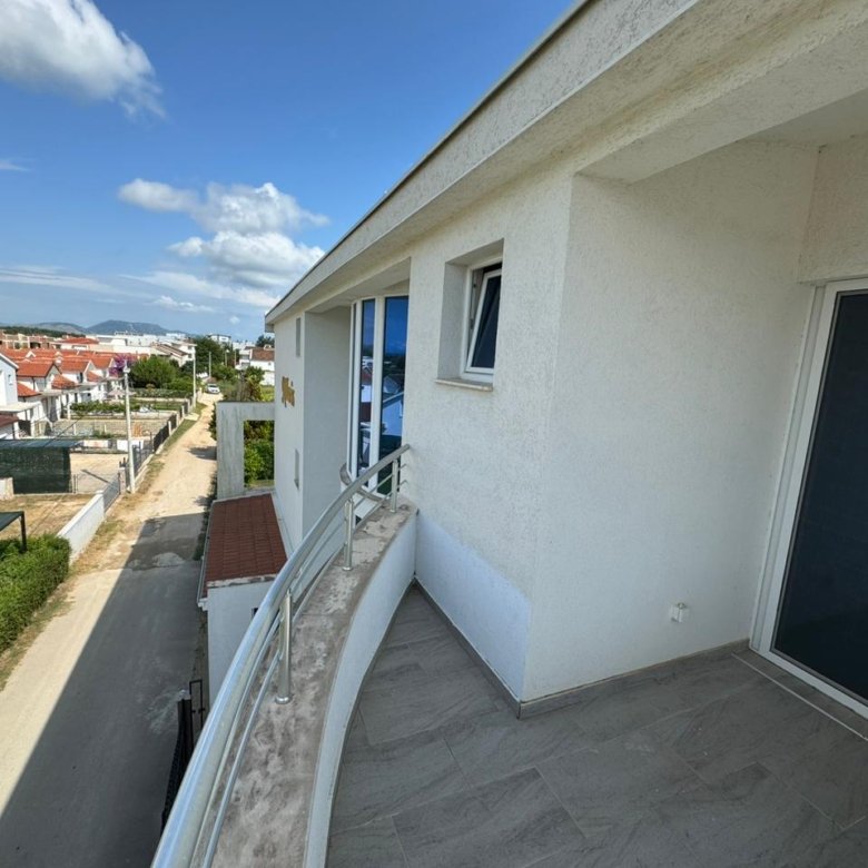 Modern second-floor balcony with glass railing overlooking red rooftops in Ulcinj, ideal for investment; by ekosphere doo.