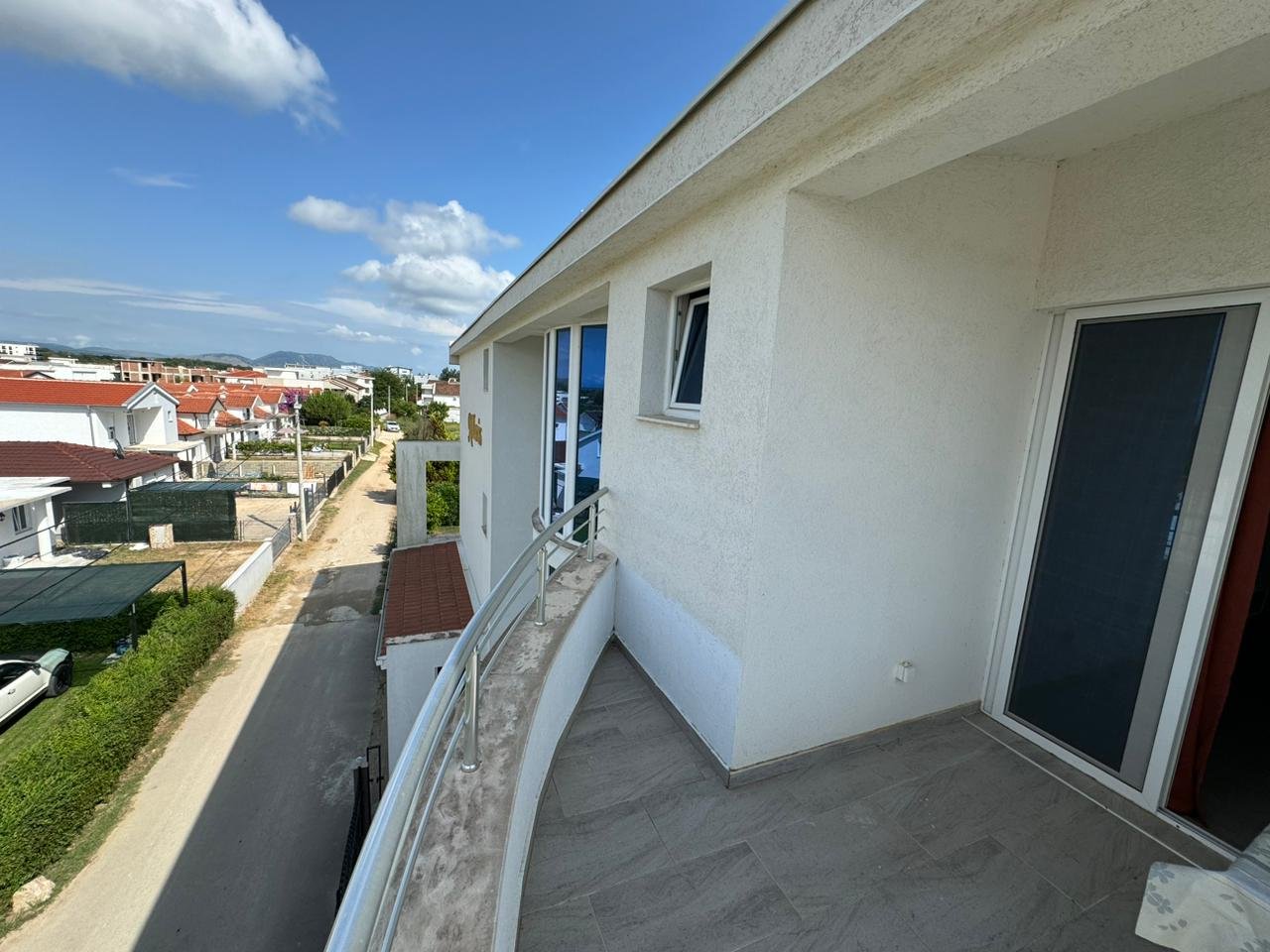 Modern second-floor balcony with glass railing overlooking red rooftops in Ulcinj, ideal for investment; by ekosphere doo.