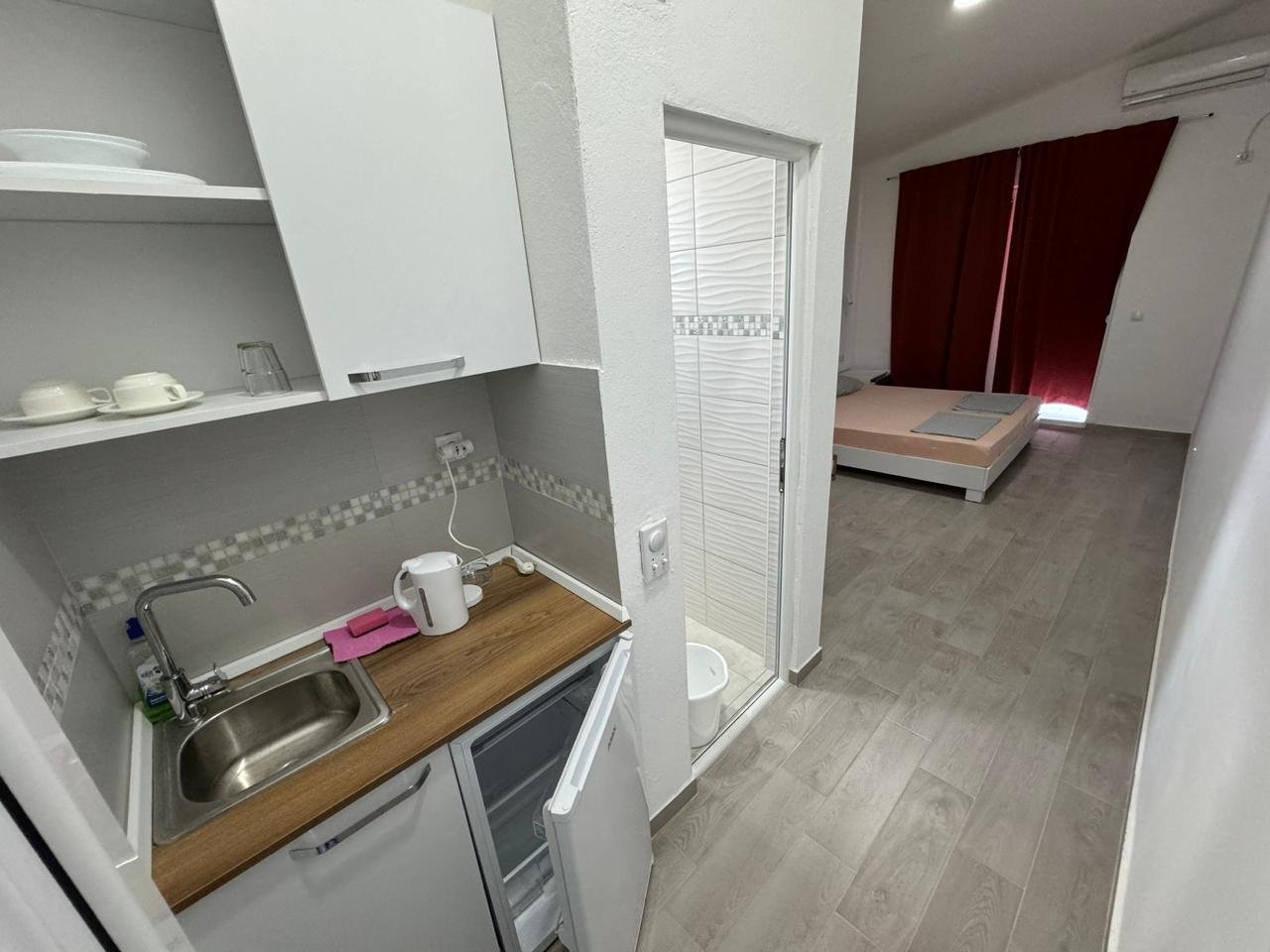 Modern studio apartment in Ulcinj with kitchenette, bed, red curtains; prime investment from Ekosphere via immorenta.me.