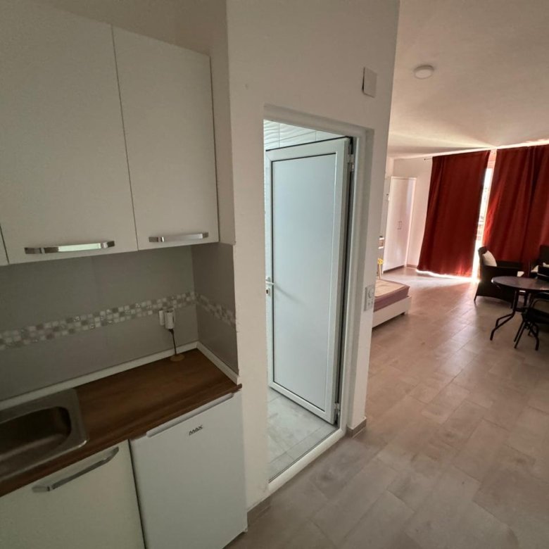 Modern kitchenette with sink and cabinets, stylish living space with bed, dining area, and vibrant red curtains&mdash;ideal Ulcinj investment from immorenta.me by ekosphere doo.