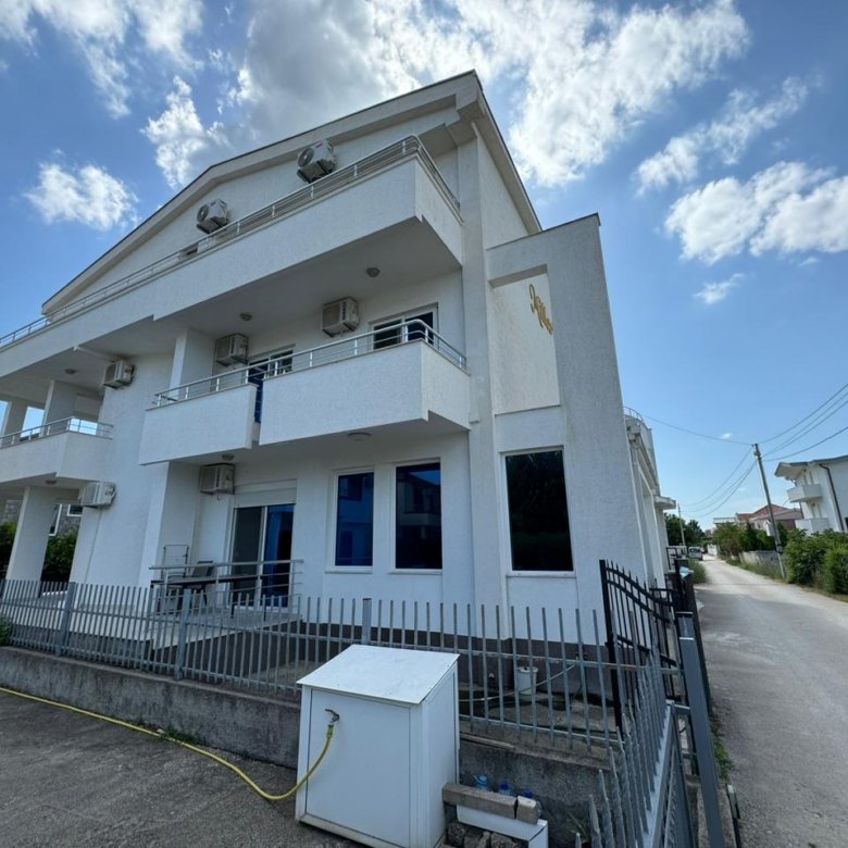 Modern white two-story home with balconies, fenced yard, and paved driveway in Ulcinj. Exclusive on immorenta.me by Ekosphere doo.